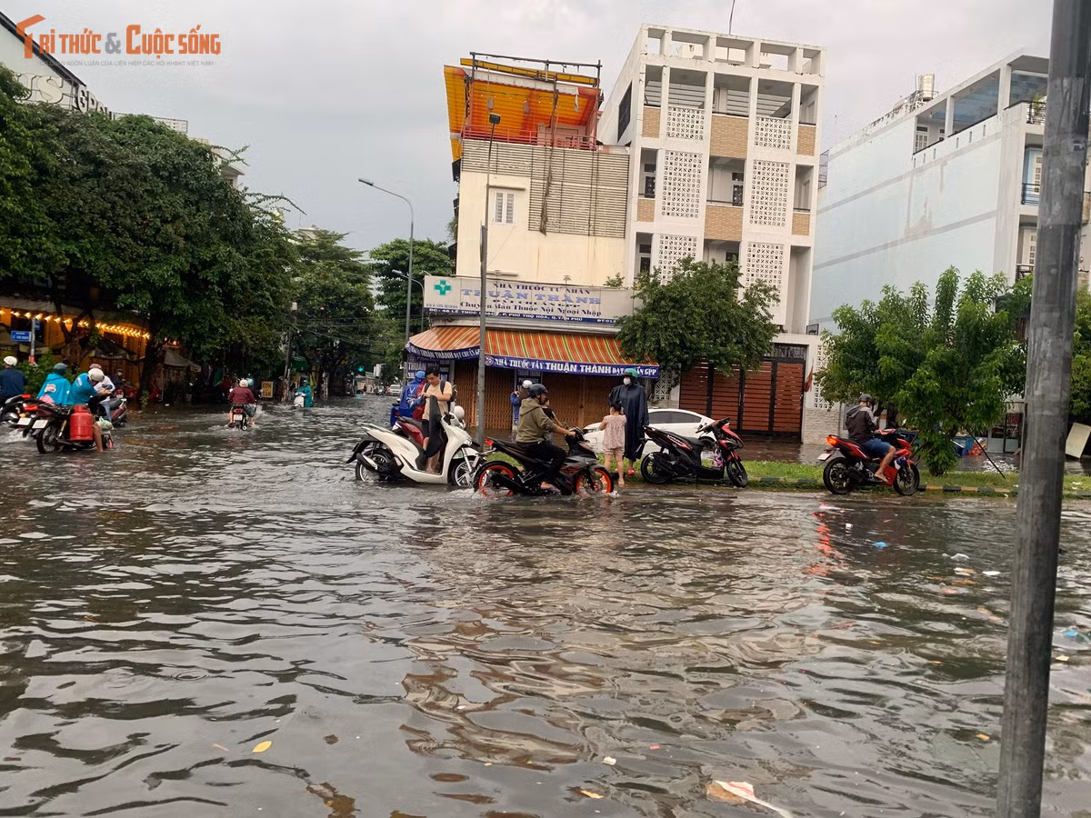 Nước ngập bao vây khắp nơi, người đi xe máy đứng ở dải phân cách chờ nước rút trên đường Lê Thúc Hoạch