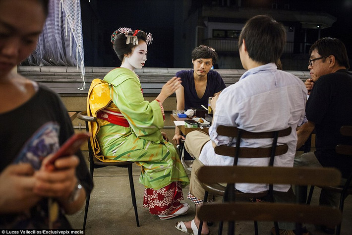 Nhóm khách hàng chăm chú lắng nghe và quan sát một geisha học việc đang trổ tài trà đạo.