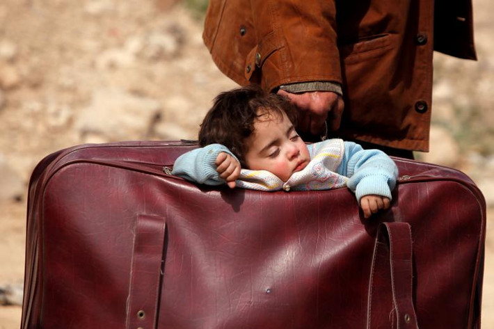 Một đứa trẻ ngủ trong một cái vali của cha mình ở làng Beit Sawa, phía đông Ghouta, Syria. Ảnh: Reuters.