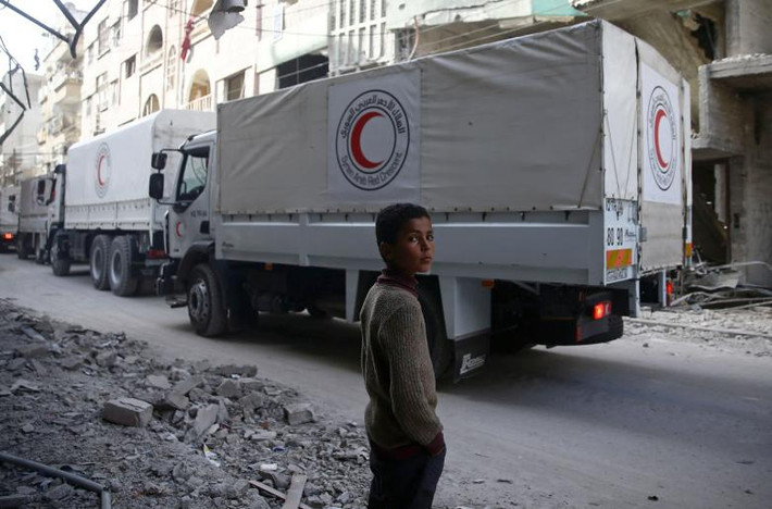 Một cậu bé đứng như một đoàn xe viện trợ của Lưỡi liềm đỏ Ả Rập Syria lái xe qua thị trấn bị bao vây Douma, Đông Ghouta, Damascus, Syria. Đến giữa tháng 4/2018, thị trấn này được Quân đội Syria giải phóng hoàn toàn. Ảnh: Reuters.