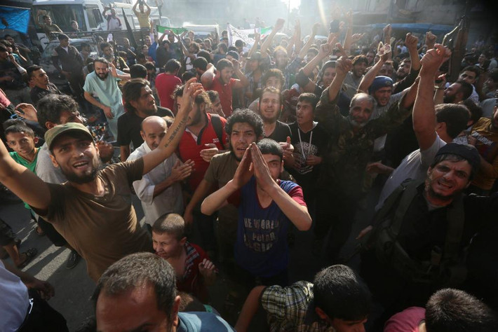 Người dân và chiến binh nổi dậy cầm cờ của hai nhóm phiến quân Syria để ăn mừng trước thông tin về việc phe nổi dậy đã phá vỡ tuyến vòng vây của quân đội chính phủ ở Aleppo.