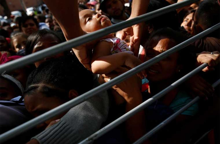 Mọi người bế một bé gái ra khỏi đám đông trong khi mẹ em xếp hàng mua tã. Ảnh Reuters