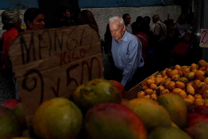 Ông lão cố gắng len qua hàng dài người dân xếp hàng để mua đồ ăn bên ngoài một siêu thị ở Venezuela. Ảnh Reuters