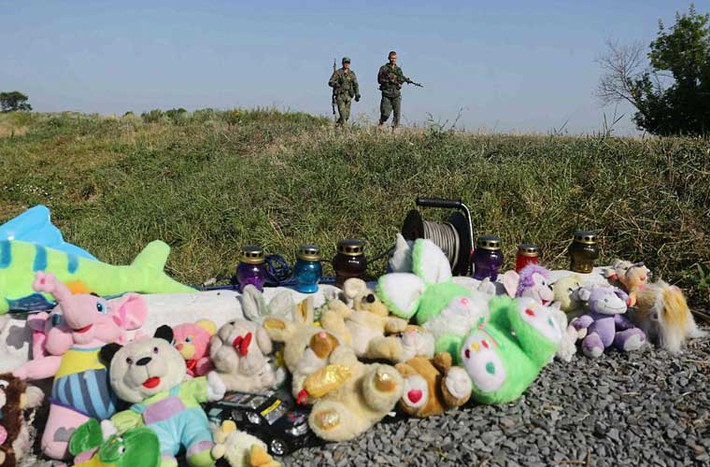 Hai dân quân thuộc phe đòi ly khai ở đông Ukraine đi ngang qua khu đất đặt gấu bông và nến tại hiện trường vụ MH17 gần làng Grabove, miền đông Ukraine.