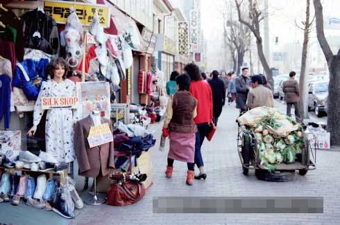 Người đàn ông kéo theo xe bán cải thảo qua các cửa hàng bán quần áo bày la liệt bên ngoài. Ảnh Sina