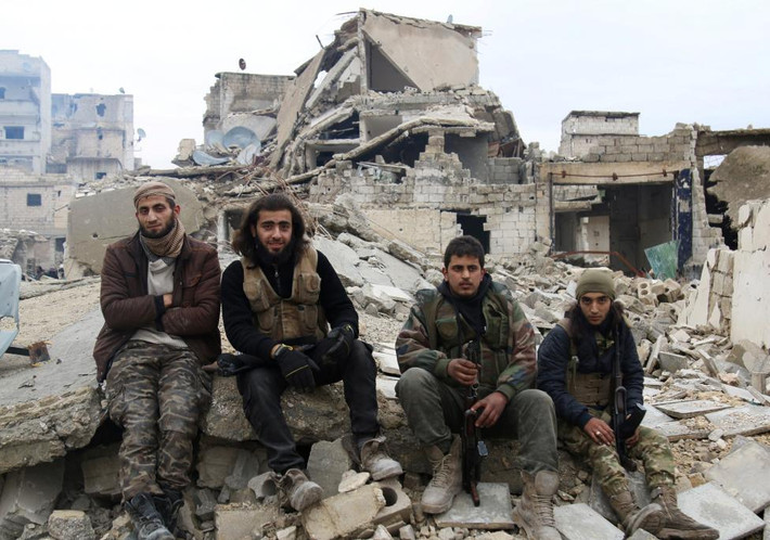 4 thành viên nổi dậy ngồi trên đống đổ nát trong lúc chờ xe rời khỏi Aleppo. Ảnh Reuters