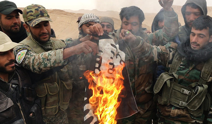Hôm 27/3, Quân đội Syria chính thức xác nhận chiến dịch giải phóng Palmyra thành công mỹ màn. Phiến quân IS đã tháo chạy sau khi chiếm được nơi này kể từ tháng 5/2015. Ảnh: Thành viên đội dân quân Đại bàng sa mạc đốt lá cờ đen của IS sau khi tháo nó xuống nóc pháo đài cổ ở Palmyra.