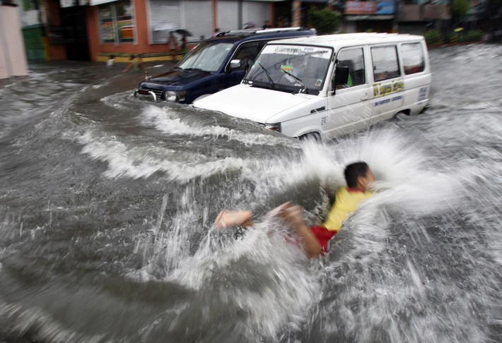 Bé trai bơi trong làn nước lũ do bão Muifa gây ra ở Manila.