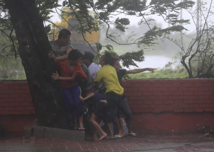 Mọi người đứng né vào một gốc cây khi có những cơn gió giật do bão Rammasun gây ra càn quét Manila hồi tháng 7/2014.