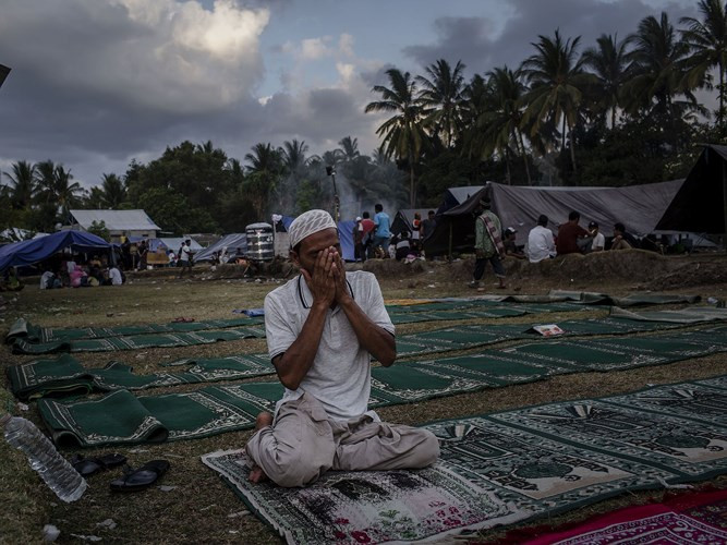 Một người đàn ông đang cầu nguyện trong một khu trú tạm ở Pemenang trên đảo Lombok, Indonesia. Gần 100 người đã thiệt mạng và ít nhất 20.000 người bị mất nhà cửa.