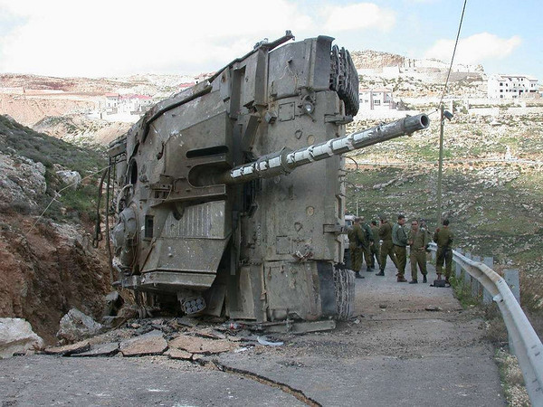 Lại một xe tăng Merkava IV khác của Israel bị lật nghiêng trên đường gây hư hại nghiêm trọng tới mặt đường. Nguồn ảnh: Rumble.