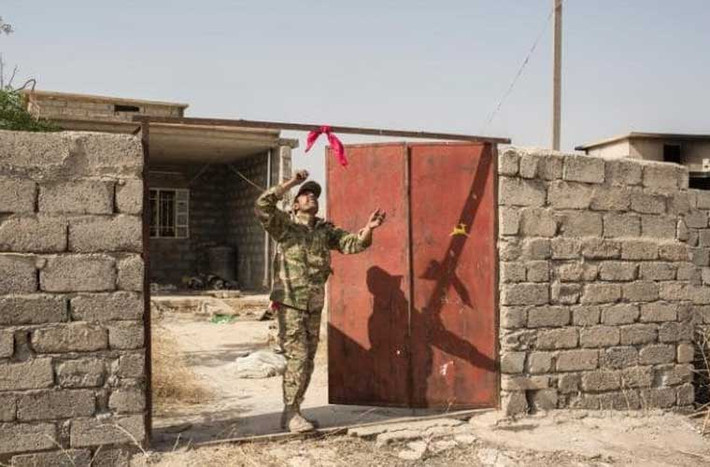 Một thành viên Peshmerga treo khăn đỏ bên ngoài một ngôi nhà để cảnh báo về các quả bom bị IS giấu trong nhà.