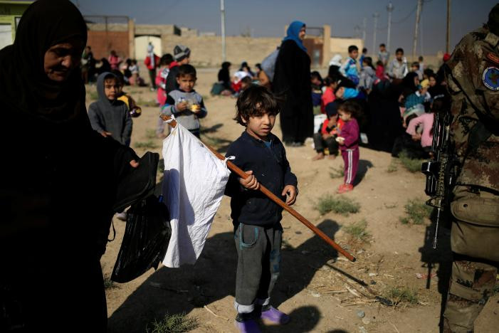 Bé trai mới chạy khỏi huyện Samah, đông Mosul đang cầm lá cờ trắng trong lúc chờ bố tại điểm chốt chặn của Lực lượng đặc nhiệm Iraq ở Kokjali, đông Mosul. Ảnh Reuters