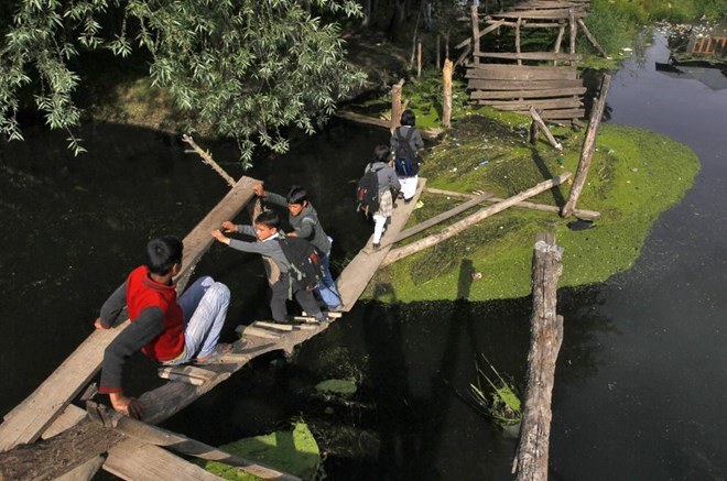 Leo qua cây cầu tạm vắt ngang qua suối trên đường từ trường về nhà ở thành phố Srinagar, Ấn Độ.