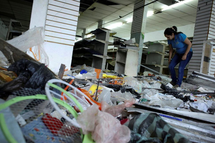 Nữ nhân viên siêu thị tìm xem còn đồ gì có thể dùng được giữa đống rác trong siêu thị mới bị cướp bóc. Ảnh Reuters