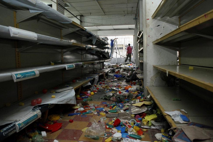 Các nhân viên đang thu dọn những gì còn sót lại trong cửa hàng sau khi bị người dân Venezuela ở La Fria xông vào cướp phá. Ít nhất 3 người chết và 405 người bị bắt giữ trong các cuộc biểu tình và cướp bóc cuối tuần qua. Ảnh Reuters