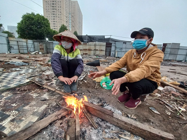Làm việc dưới trời lạnh, chị Huê và người đồng hương Nông Thị Nhung đốt củi sưởi ấm, hơ tay cho bớt giá. Các chị cho biết năm nay sẽ phải về quê sớm hơn một tuần để đủ thời gian cách ly phòng dịch Covid-19 theo quy định của địa phương. Vụ làm Tết, vì thế, cũng gấp gáp, phấp phỏng hơn.