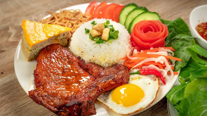 Sau bữa sáng nhẹ nhàng, bữa trưa sẽ là thời điểm lý tưởng để “thưởng” món cơm tấm – món ăn được mệnh danh là “đặc sản đường phố” của người TP HCM. Một đĩa cơm tấm hoàn chỉnh gồm hạt cơm tơi, miếng sườn nướng thơm phức, trứng ốp la béo ngậy, bì, chả và không thể thiếu chén nước mắm pha chua ngọt đậm đà. Ảnh VinWonder