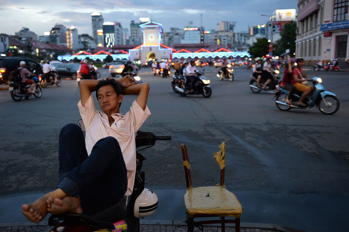 Người đàn ông làm nghề xe ôm ngả lưng trên xe tại một ngã tư đông đúc vào lúc chiều tối. Ảnh USN