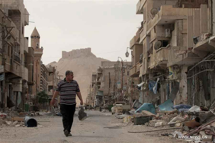 Người đàn ông đi bộ trên con phố với hai bên đường là các ngôi nhà hư hại ở Palmyra.