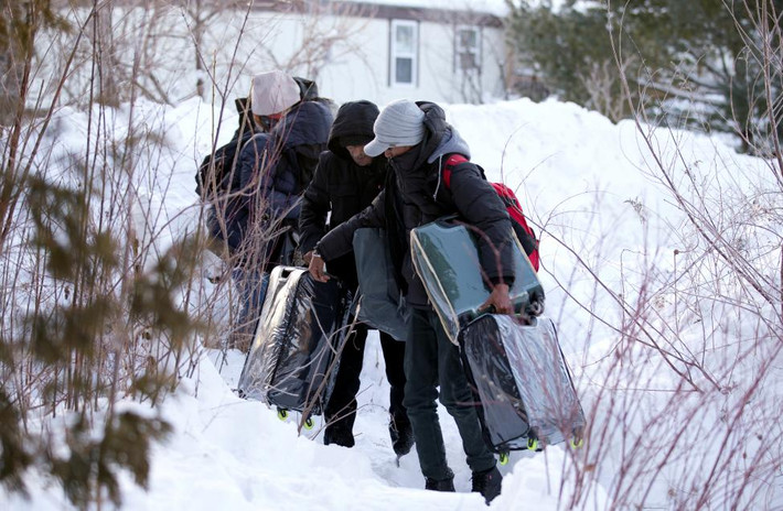 Một nhóm những người di cư khệ nệ bê đồ đạc trong lúc vượt biên trái phép sang Canada. Ảnh Reuters