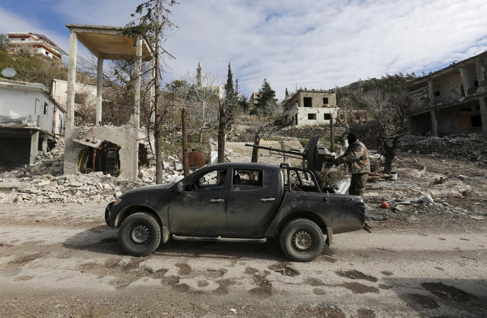 Lính chính phủ Syria đứng trên một chiếc xe di chuyển trên con đường ở thị trấn Rabiya.