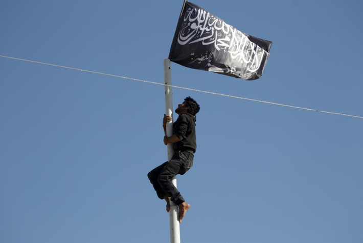 Một thành viên của Mặt trận Nusra (thuộc chi nhánh của tổ chức khủng bố al-Qaeda) trèo lên cột để treo cờ của phong trào này nằm ở một quảng trường trung tâm thành phố Ariha sau khi liên minh các nhóm nổi dậy giành được khu vực trên.