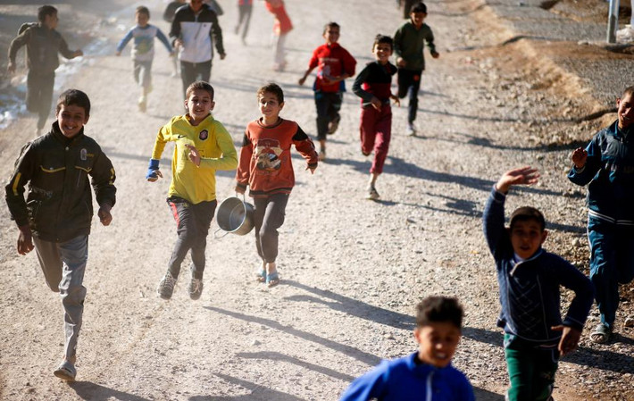 Các em bé Iraq đang chạy theo sau một xe tải chở đồ ăn cứu trợ tại một điểm phân phát trong trại tị nạn Khazer. Ảnh Reuters