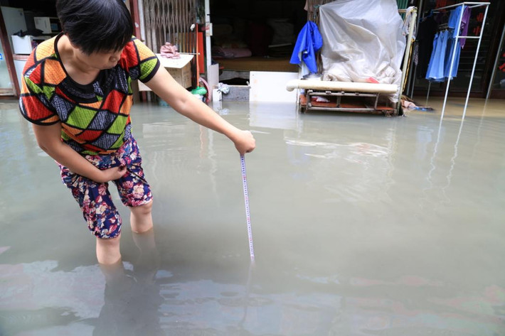 Người phụ nữ mang thước dây ra đo mực nước mưa ở ngoài đường.