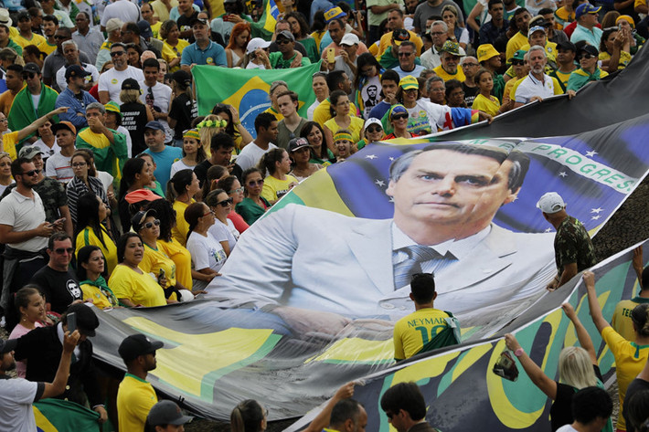Người ủng hộ cầm banner khổng lồ in hình tân Tổng thống Brazil Jair Bolsonaro trong lễ nhậm chức của ông tại Brasilia ngày 1/1. Hơn 100.000 người đã có mặt tại thủ đô để tham dự sự kiện. Nhiều người tin rằng nhà dân túy cực hữu Bolsonara có thể giải cứu đất nước thoát khỏi tham nhũng bào mòn, tội phạm bạo lực gia tăng và kinh tế ảm đạm. Ảnh: AP.