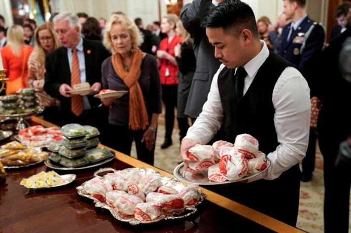Nhân viên phục vụ đặt thêm bánh hamburger vào khay.