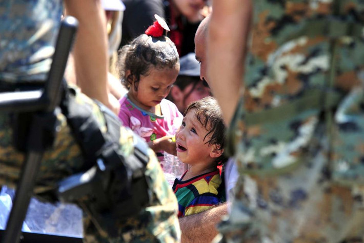 Đứa trẻ tị nạn Syria khóc to khi nhìn lên một sĩ quan mặc đồng phục thuộc lực lượng đặc nhiệm Macedonia gần Gevgelija.