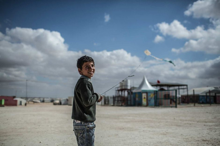 Bé trai mỉm cười trong lúc thả diều tại trại tị nạn Zaatari.