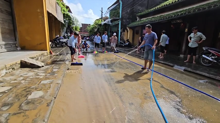 Hàng chục người dân và đội quy tắc đô thị tập trung dọn bùn trên tuyến đường Nguyễn Thái Học sau khi nước rút.