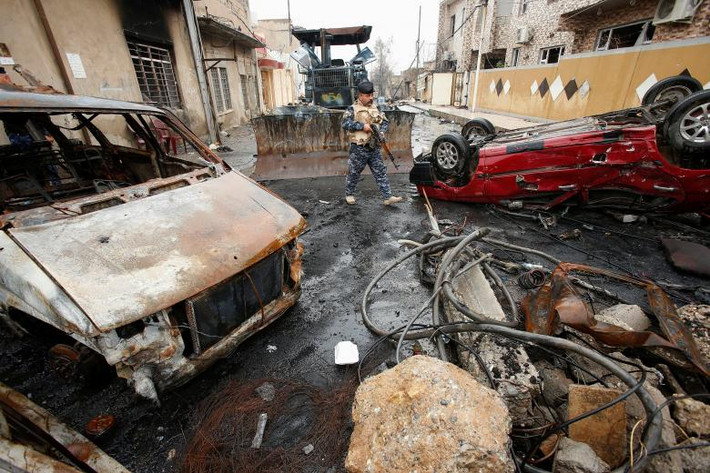 Một người cảnh sát liên bang Iraq đi ngang qua các xe bị cháy rụi ở Mosul. Ảnh Reuters