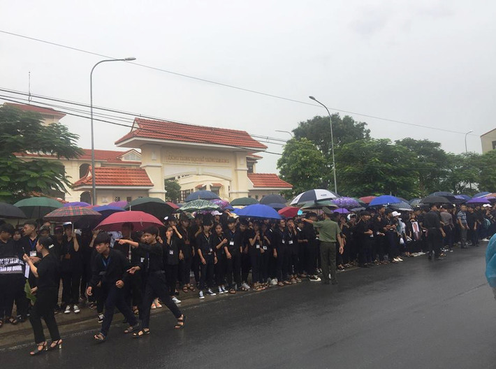 Các cháu học sinh mặc quần áo đen, nghiêm trang đứng đợi dưới trời mưa. Ảnh Hải Ninh