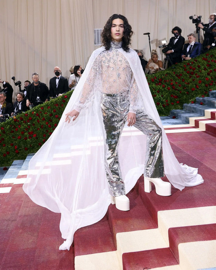 Khoảnh khắc Conan Gray tham dự Met Gala giúp anh lọt vào mắt xanh của nhiều tạp chí thời trang. Giới mộ điệu ca ngợi gu thời trang tinh tế của giọng ca 24 tuổi. Conan Gray diện bộ trang phục do Valentino thiết kế. Mẫu áo choàng voan trắng kết hợp cùng áo xuyên thấu tô điểm thêm chi tiết kim loại và quần ống rộng lấp lánh. Ảnh: People