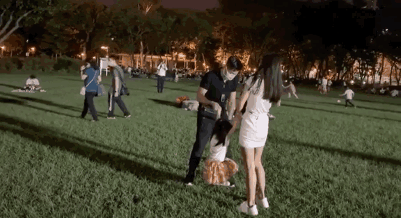 Hai bố mẹ nắm tay hai con gái vui đùa trên một bãi cỏ rộng.