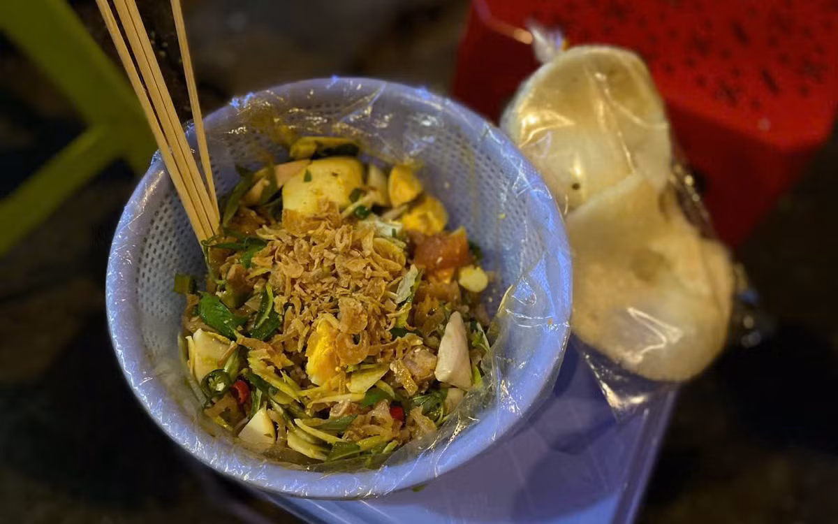 Ngay khu vực ga tàu lửa Sài Gòn, đoạn 1 Nguyễn Thông (phường Xuân Hòa), không khí về đêm lúc nào cũng rộn ràng. Những gánh tré trộn, bánh tráng trộn nối nhau sáng đèn từ chiều tối đến tận rạng sáng hôm sau, trở thành điểm hẹn quen thuộc của người trẻ. Một phần tré trộn đầy đặn, ăn kèm bánh phồng giòn tan, vị chua chua, cay cay hòa cùng mùi rau thơm rất “bắt miệng”. Bánh tráng trộn giá mềm, dễ mua mang về, càng khiến khu phố nhỏ này thêm tấp nập mỗi khi đêm về. Ảnh Thái Bảo