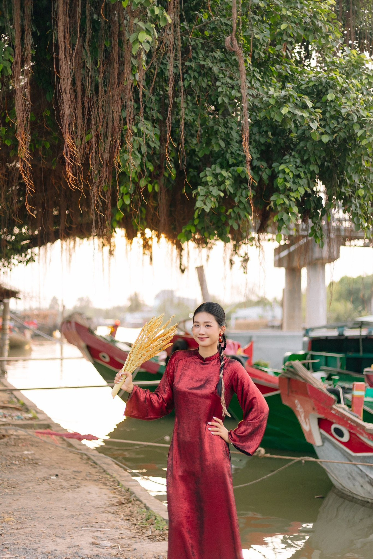 Màu đỏ trầm của áo dài hòa quyện cùng sắc nắng, sắc xơ dừa và màu xanh của sông nước, khiến từng khung hình vừa mang nét duyên quê, vừa đậm chất nghệ thuật.