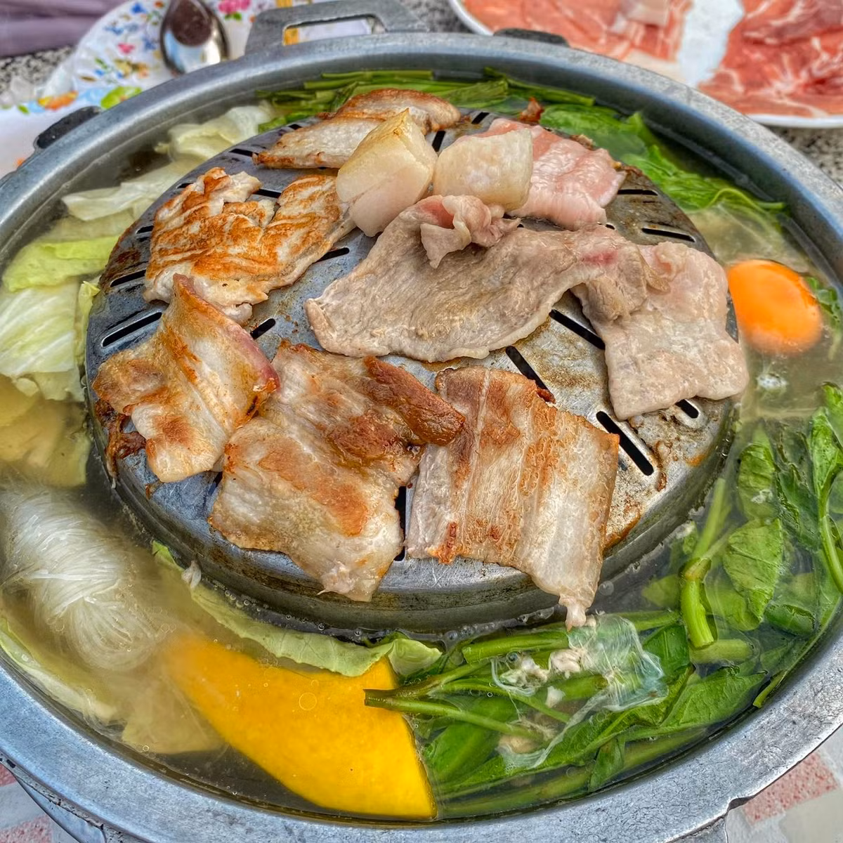 Một món ăn vừa hấp dẫn về hương vị, vừa lạ mắt về cách trình bày là Lẩu Xìn Đạt. Đúng như tên gọi, món này kết hợp nướng và lẩu: đồ nướng trên bếp sẽ rơi xuống nước lẩu bên dưới, tạo nên vị đậm đà khó quên. Nguyên liệu đa dạng từ thịt bò, thịt ba rọi, vú dê đến hải sản như mực, bạch tuộc, ăn kèm rau và bún tươi. Phần nước lẩu có thể là vị Thái chua cay hoặc nước xương hầm thanh ngọt, giúp món ăn hài hòa giữa nướng và lẩu. Ảnh VietLao