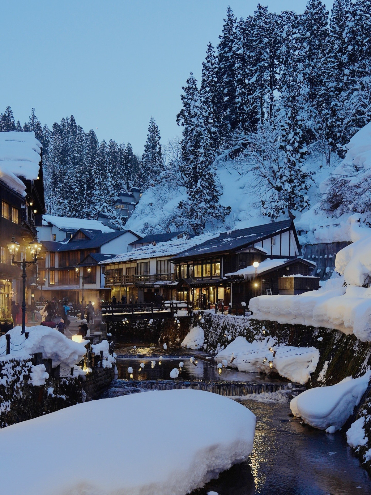 Vào mùa đông, khung cảnh Ginzan Onsen trở nên quyến rũ hơn bao giờ hết. Tuyết rơi dày phủ trắng mái nhà, lan can và những bậc đá ven sông, trong khi ánh đèn vàng từ các ryokan phản chiếu xuống mặt nước, tạo nên một không gian vừa ấm áp vừa lãng mạn. Chính vẻ đẹp này đã khiến nhiều người liên tưởng đến thế giới huyền ảo trong bộ phim hoạt hình kinh điển Spirited Away của đạo diễn Hayao Miyazaki – tác phẩm từng đoạt giải Oscar. Cũng vì thế, Ginzan Onsen thường được du khách ưu ái gọi bằng cái tên “Vùng đất linh hồn” ngoài đời thực.