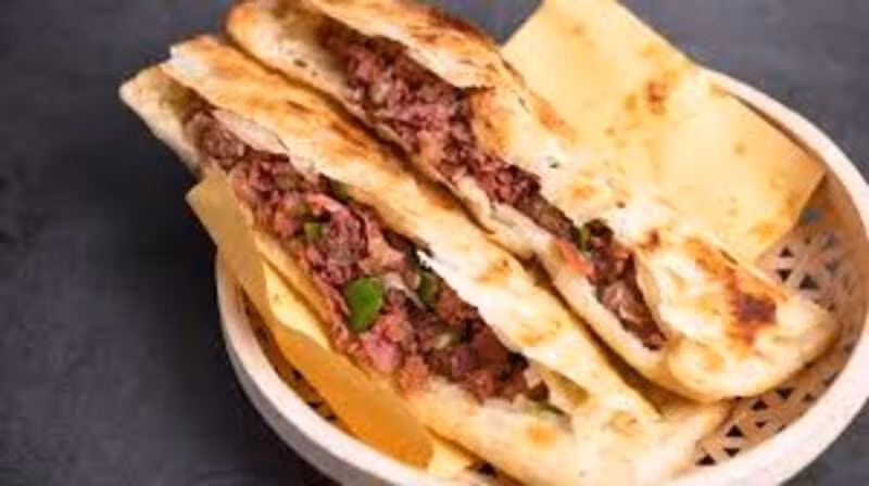 Đậm chất dân dã không kém là bánh nướng kẹp thịt hầm – món ăn từng gắn liền với bữa sáng của người Bắc Kinh xưa. Thịt heo được hầm mềm, tẩm ướp đậm vị rồi kẹp trong bánh nướng nóng giòn, mang lại cảm giác chắc bụng và quen thuộc. Ảnh MIA