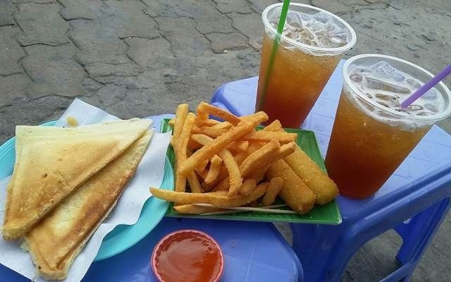 Rời Nguyễn Thông, nhiều bạn trẻ lại tìm đến Trà chanh &amp; Hotdog Hàng Xanh để tiếp tục cuộc vui. Quán vỉa hè giản dị nhưng luôn đông khách nhờ những chiếc hotdog nóng hổi, đặc biệt là phiên bản nhân phô mai béo ngậy. Chỉ cần một ly trà chanh mát lạnh, vài chiếc ghế nhựa ven đường, thực khách đã có thể ngồi lại rất lâu, vừa ăn vừa ngắm dòng xe cộ và cảm nhận rõ nét nhịp sống sôi động của Sài Gòn về đêm. Ảnh Riviu