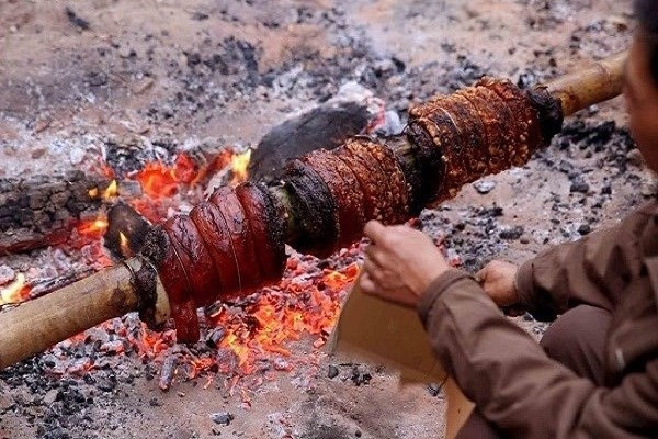 Khi mỡ chảy ra, lớp bì được châm nhẹ bằng que tre cho phồng giòn, phát ra tiếng lách tách. Trước khi hoàn tất, thịt được phết thêm mật ong để tạo màu vàng óng và mùi thơm hấp dẫn. Toàn bộ quá trình quay kéo dài khoảng 6 tiếng. Ảnh Đình Châu