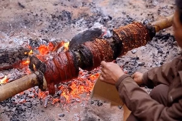 Khi mỡ chảy ra, lớp bì được châm nhẹ bằng que tre cho phồng giòn, phát ra tiếng lách tách. Trước khi hoàn tất, thịt được phết thêm mật ong để tạo màu vàng óng và mùi thơm hấp dẫn. Toàn bộ quá trình quay kéo dài khoảng 6 tiếng. Ảnh Đình Châu