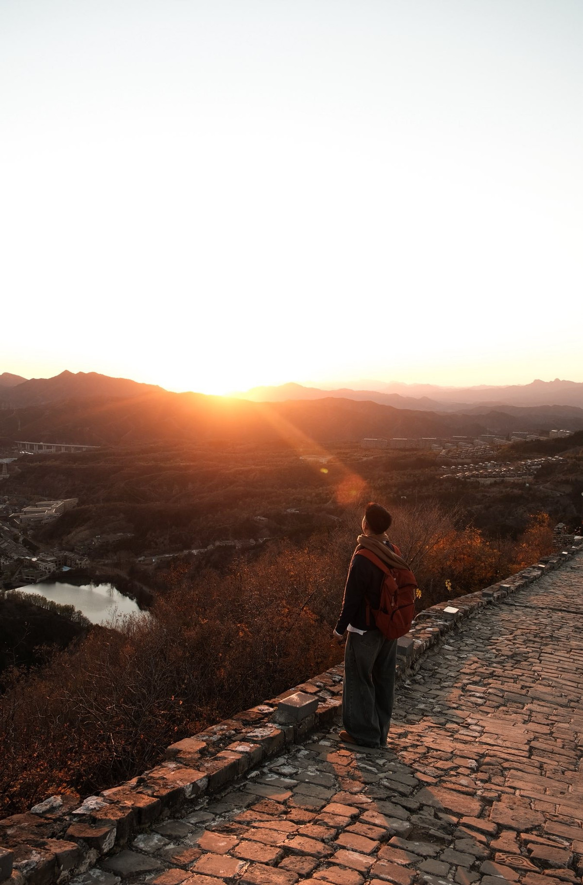 Từ khoảng cách xa, Vạn Lý Trường Thành không phô trương mà lặng lẽ hiện hình giữa núi rừng, khi ẩn trong sương mờ, lúc nổi bật trên nền trời xanh thẳm. Những đoạn tường thành nối tiếp nhau bám theo sống núi, vượt qua triền dốc dựng đứng, tạo nên một đường nét mềm mại nhưng đầy uy lực giữa thiên nhiên khắc nghiệt.