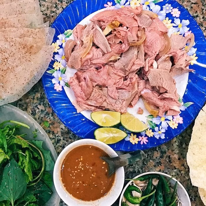 Để cảm nhận trọn vẹn hương vị, du khách nên ăn đúng chuẩn người địa phương: vắt chút nước cốt chanh lên miếng thịt, xếp lần lượt rau sống, chuối xanh, đu đủ, rồi miếng bê thui lên bánh tráng, cuộn chặt tay và chấm vào chén nước mắm cá cơm pha sẵn. Ảnh Vinpearl