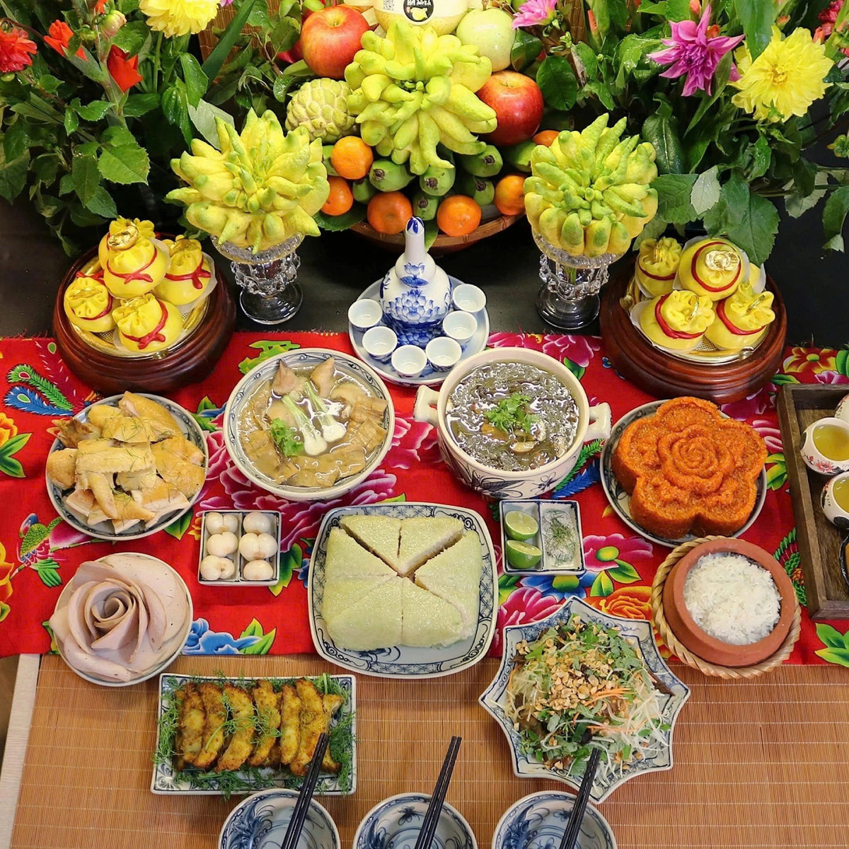 Mâm cỗ rực rỡ sắc màu với gà luộc, tôm hấp, chả cắt hoa, nem rán, thịt đông, xôi gấc tạo hình, bánh chưng, canh nóng và các món nộm, dưa góp. Xen kẽ là hoa tươi, rượu cúng và mâm hoa quả, tạo không gian trang nghiêm, ấm cúng. Ảnh Internet