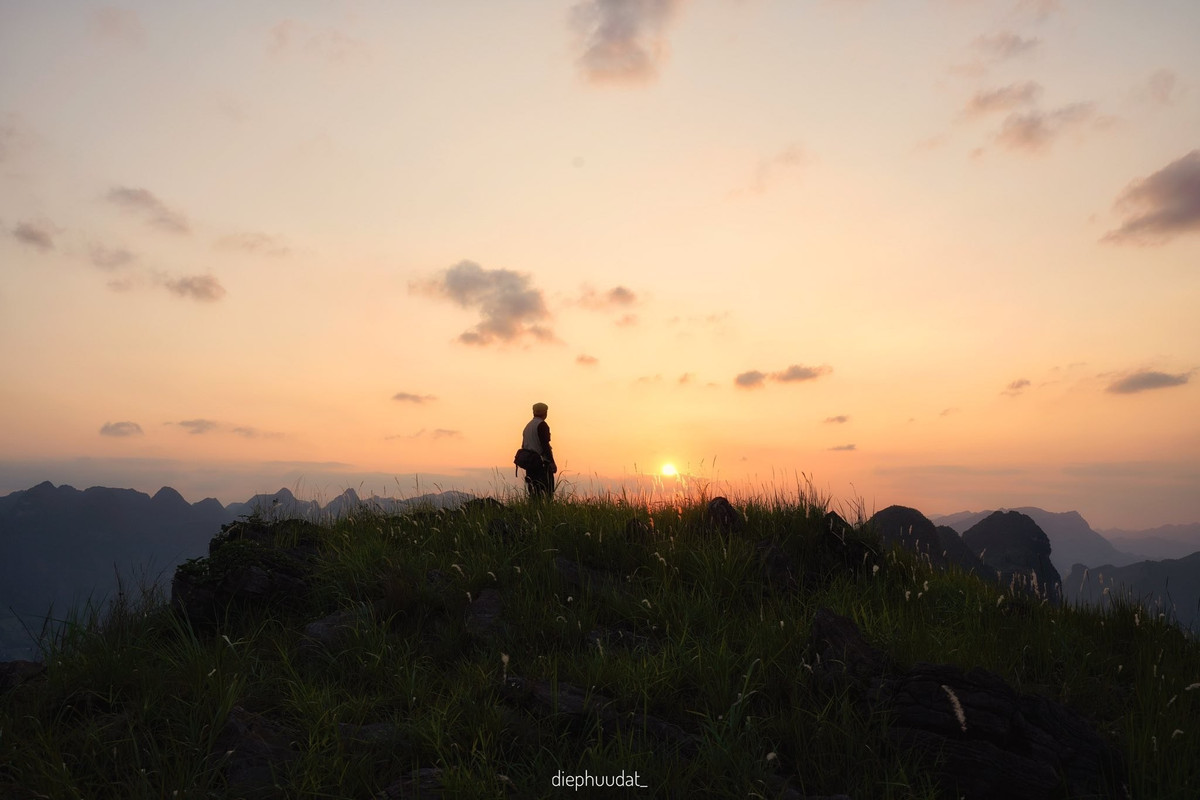 Từ trên cao nhìn xuống, sông Nho Quế hiện ra như một dải lụa xanh ngọc, uốn lượn giữa lòng núi đá. Khi mặt trời lặn dần, mặt nước phản chiếu sắc vàng cam rực rỡ, những tia nắng cuối cùng như níu giữ từng đường cong của sông, từng vách đá sừng sững. Cảnh vật lúc này như chậm lại, lắng đọng cùng bước chân người lữ khách. Ảnh Diệp Hữu Đạt